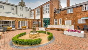 A courtyard with a fountain, seating areas, and a brick building with large windows. - The Northwick Arms (Evesham)