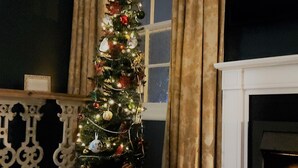 A Christmas tree decorated with ornaments and lights, positioned next to a fireplace with a lit fire. - The Northwick Arms (Evesham)