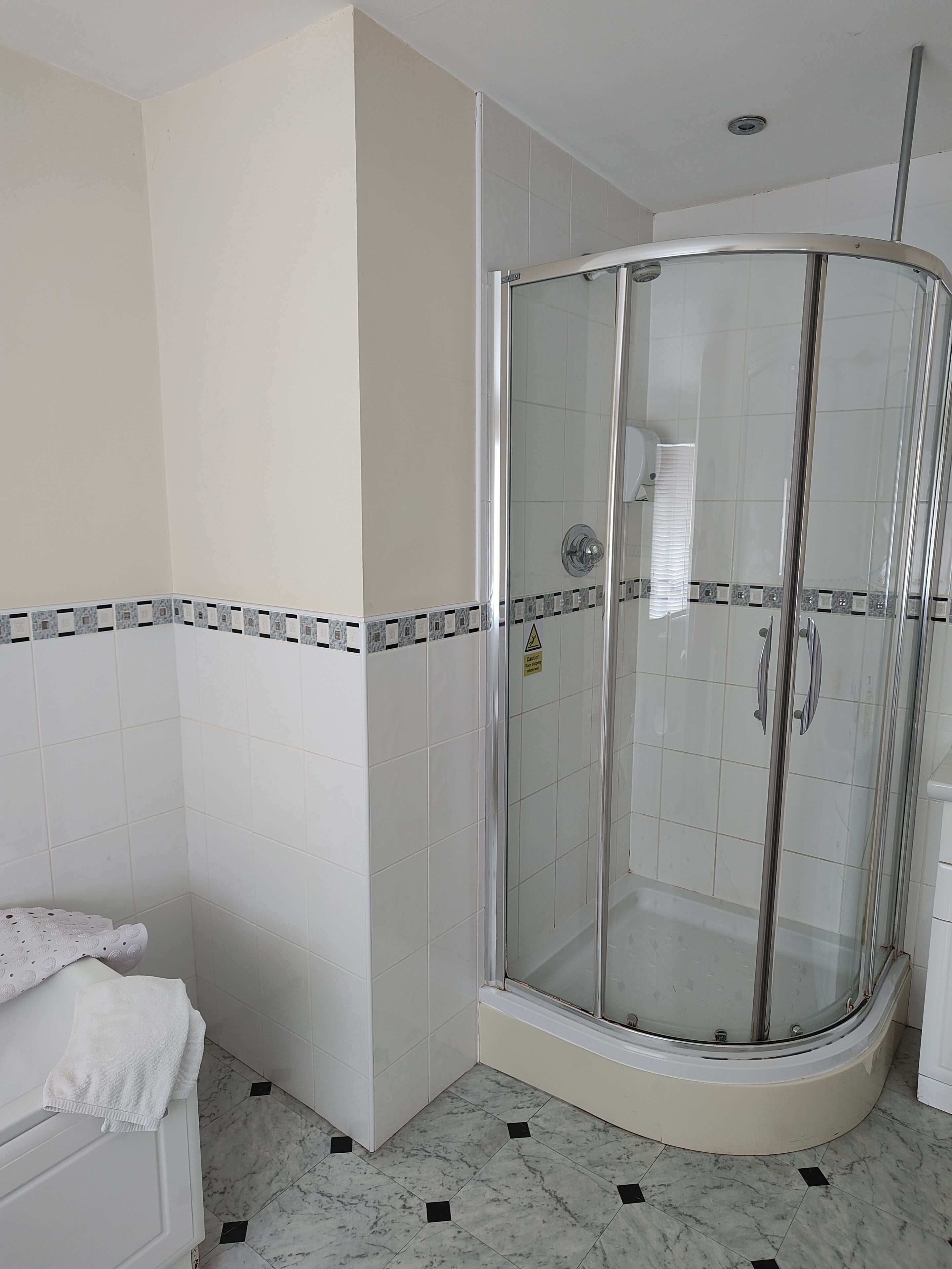 Un baño moderno con ducha de vidrio, paredes de azulejos blancos y suelo de mármol.