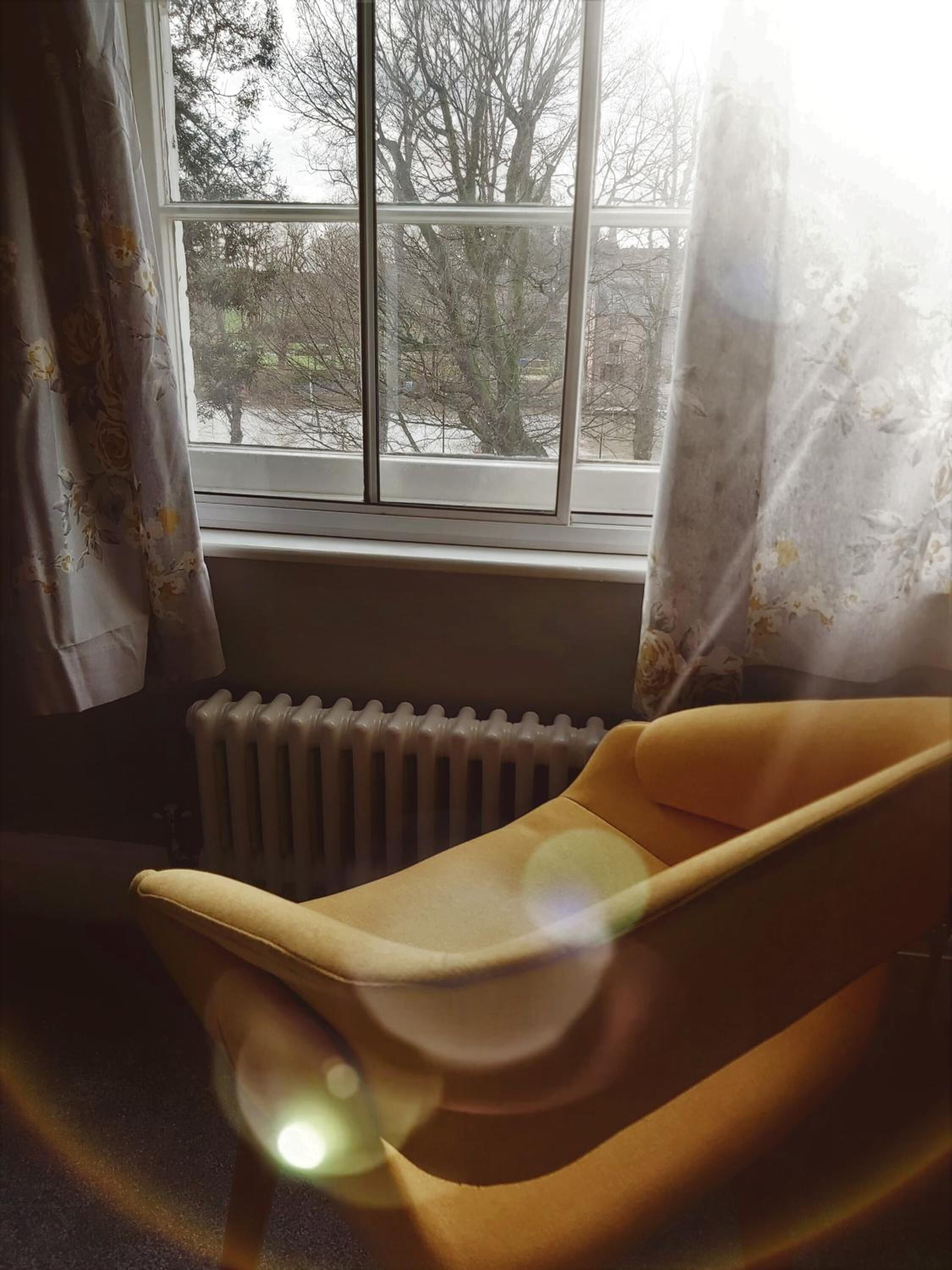 A room with a window, a radiator, and a yellow chair.
