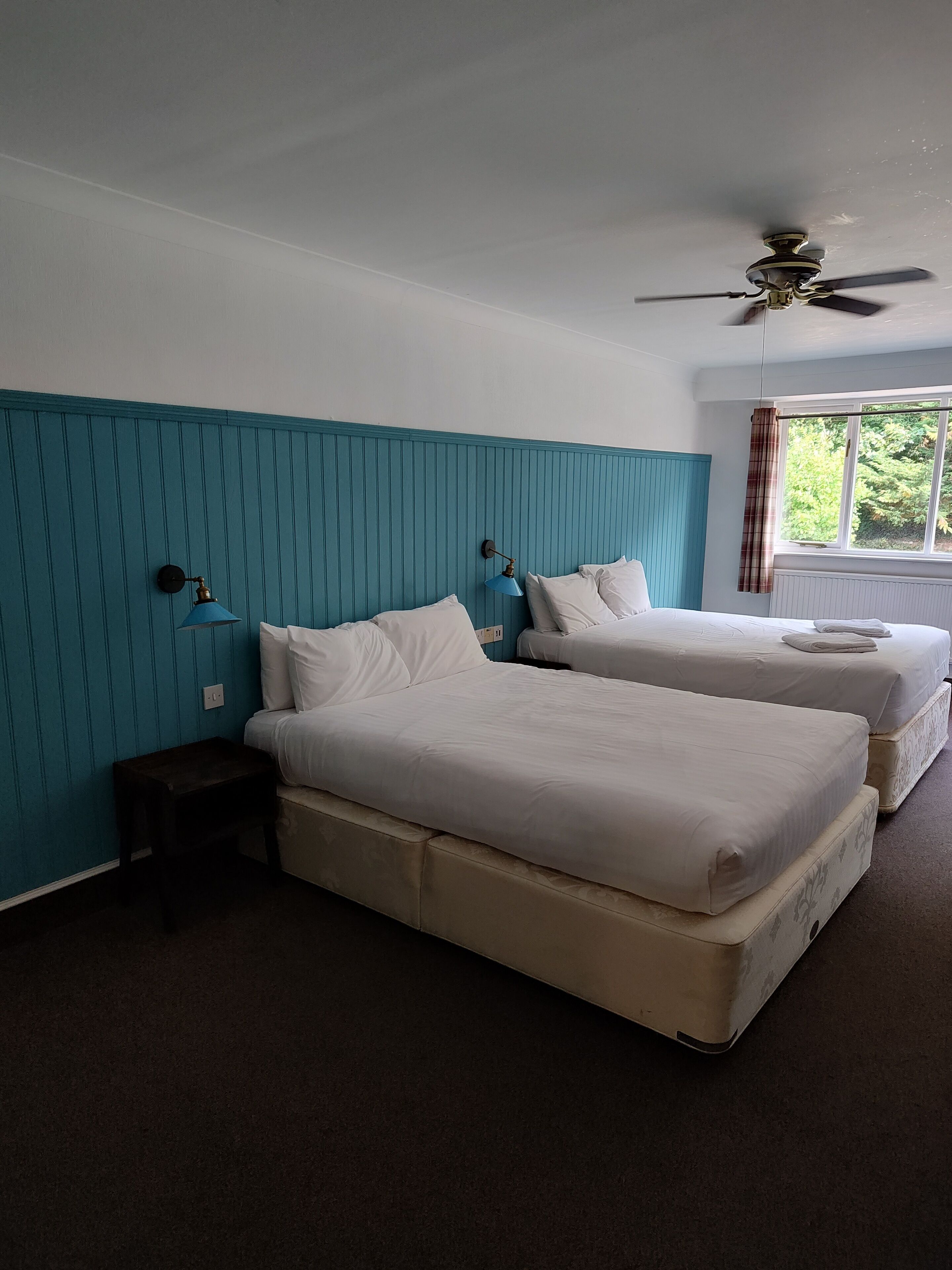 Une chambre d’hôtel avec deux lits, un ventilateur de plafond et une fenêtre avec des rideaux.
