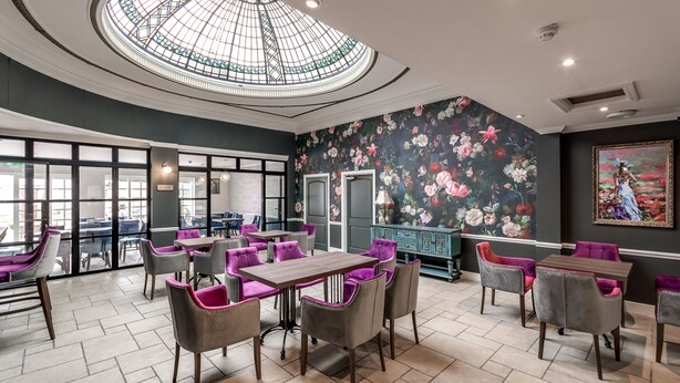 A restaurant with a large glass dome ceiling, floral wallpaper, and purple and grey chairs. - The Northwick Arms (Evesham)