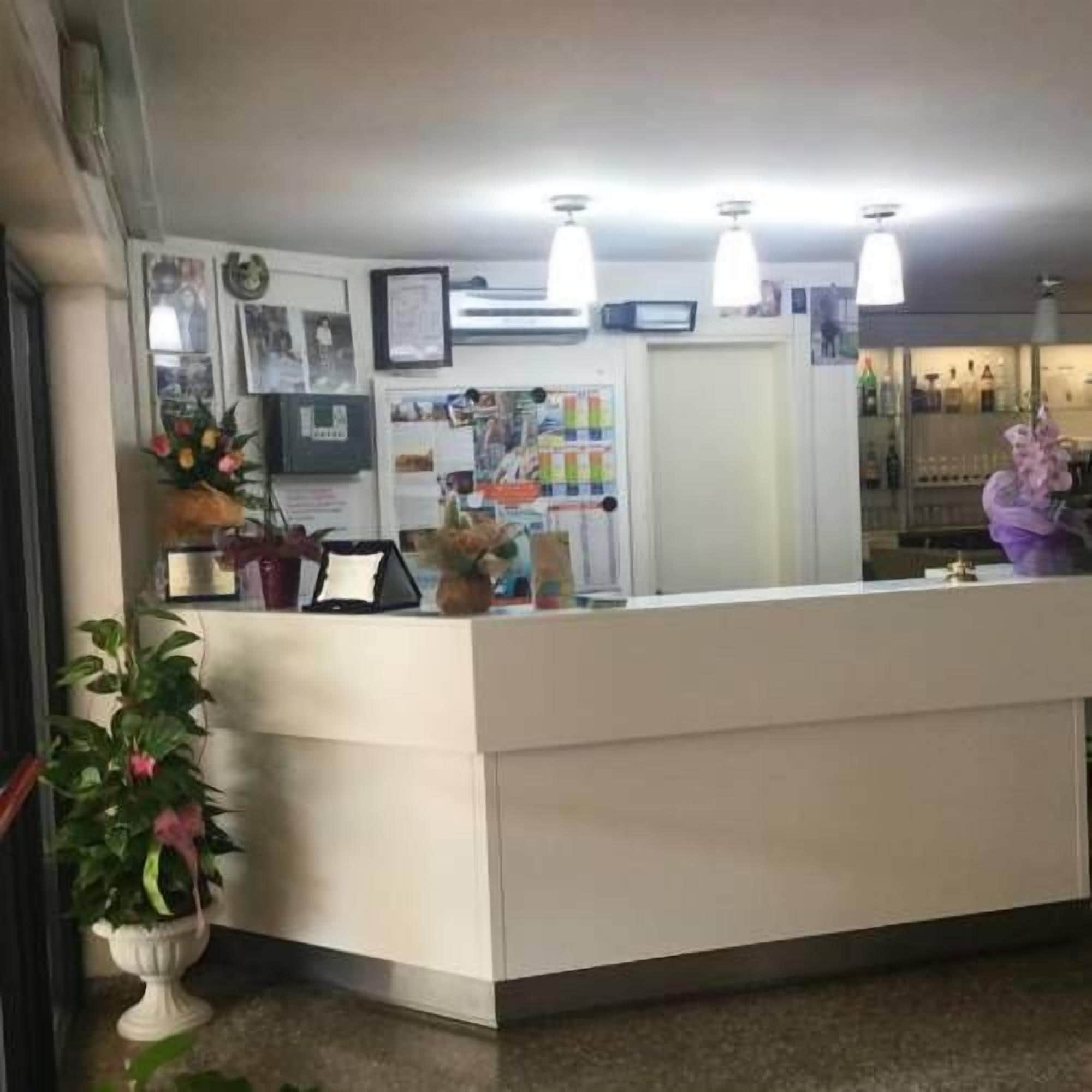 Una reception con un bancone bianco, una pianta in vaso e quadri appesi al muro.
