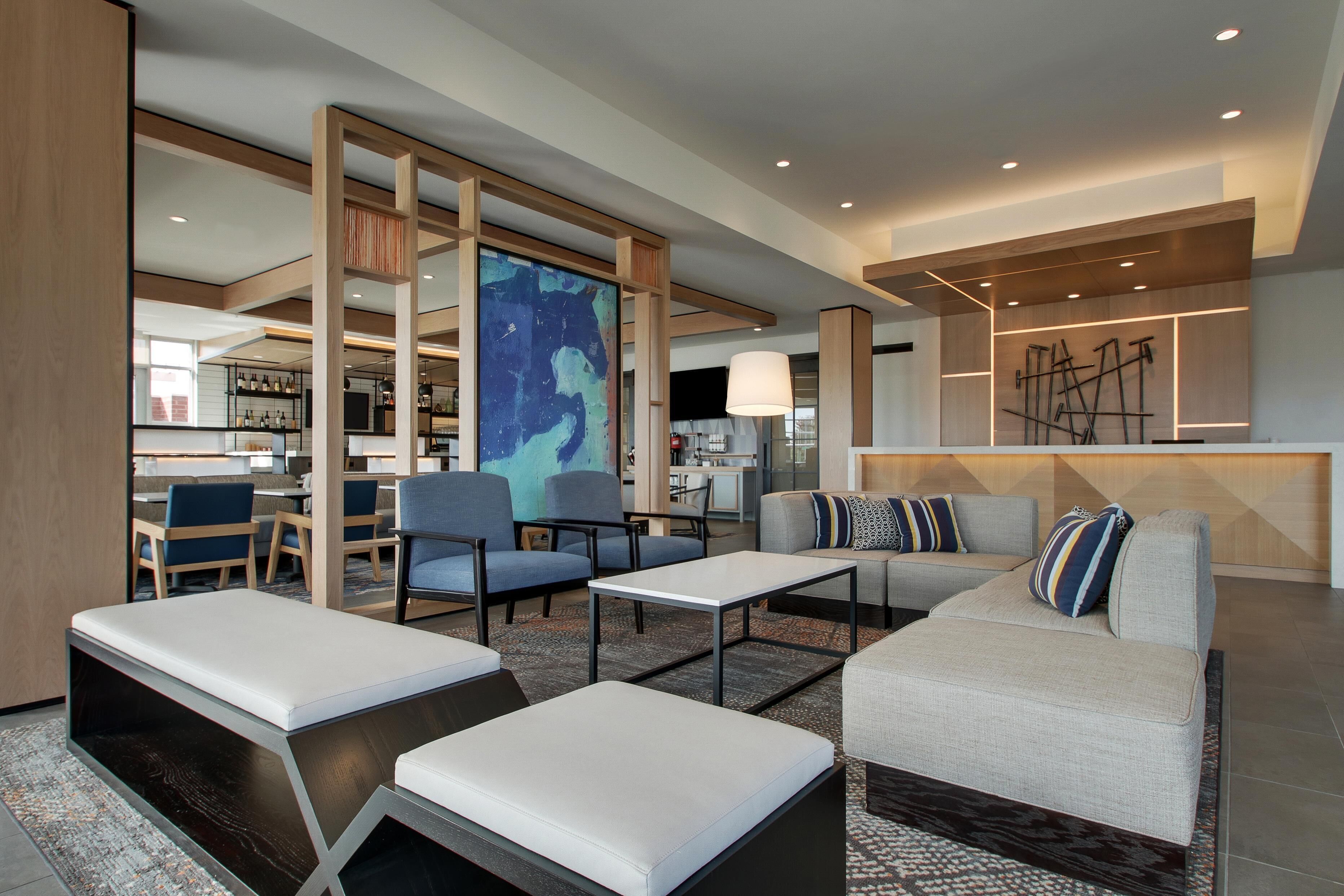 A modern hotel lobby with seating areas, a large abstract painting, and a bar area.