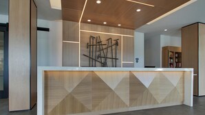 A reception desk with a geometric wood panel design, a wooden ceiling with recessed lighting, and a modern interior.