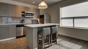 A modern kitchen with a central island, stainless steel appliances, and a large window.