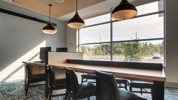 Un espace de bureau moderne doté d’un grand bureau, de plusieurs chaises, d’un éclairage suspendu et d’une grande fenêtre offrant une vue sur l’extérieur.