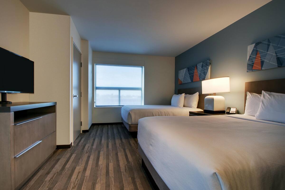 A hotel room with two beds, a TV, a desk, and a window.