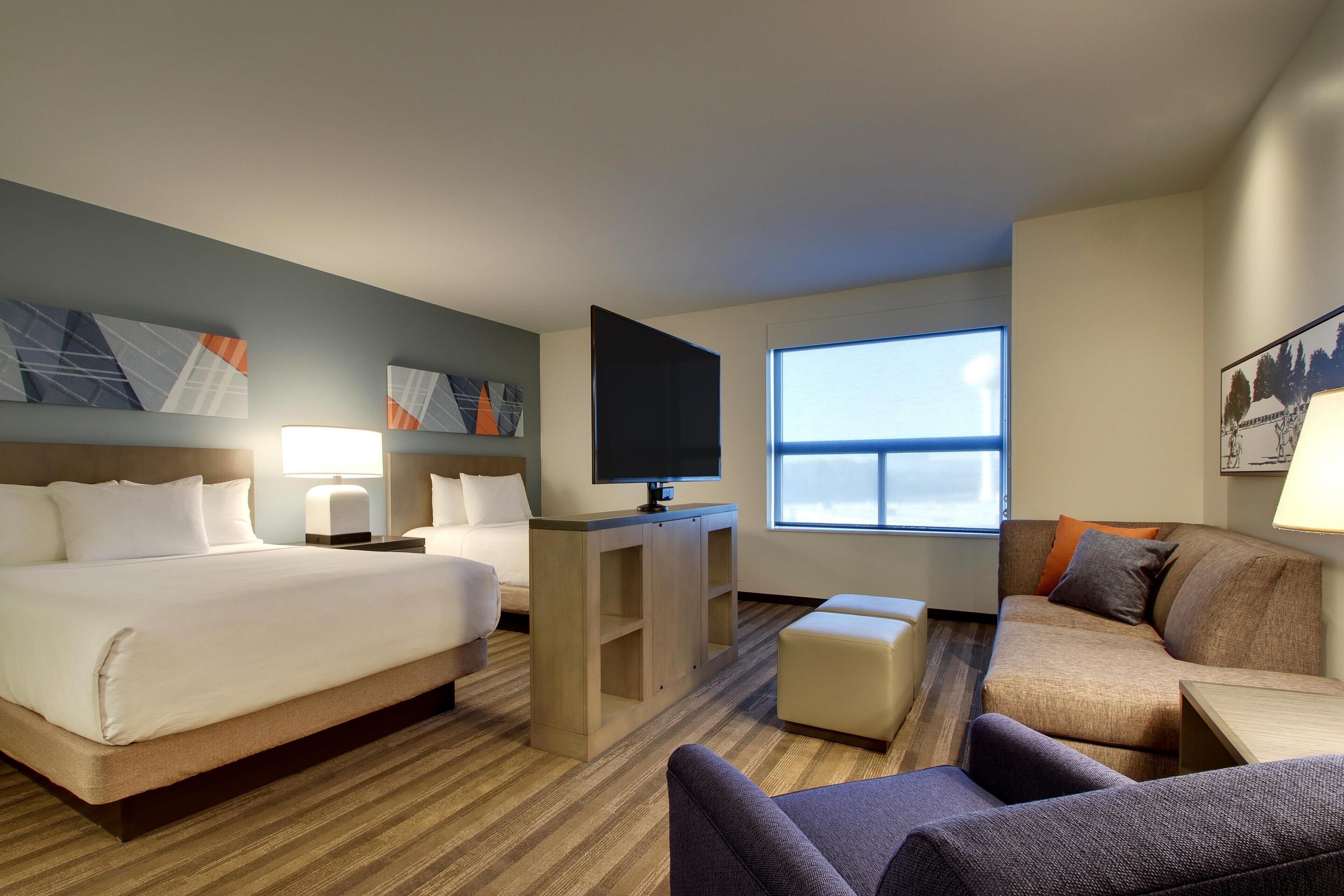 A hotel room with a bed, a sofa, a TV, and a window.