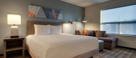 Habitación de hotel con una cama grande, mesitas de noche, un escritorio, una silla y una ventana.