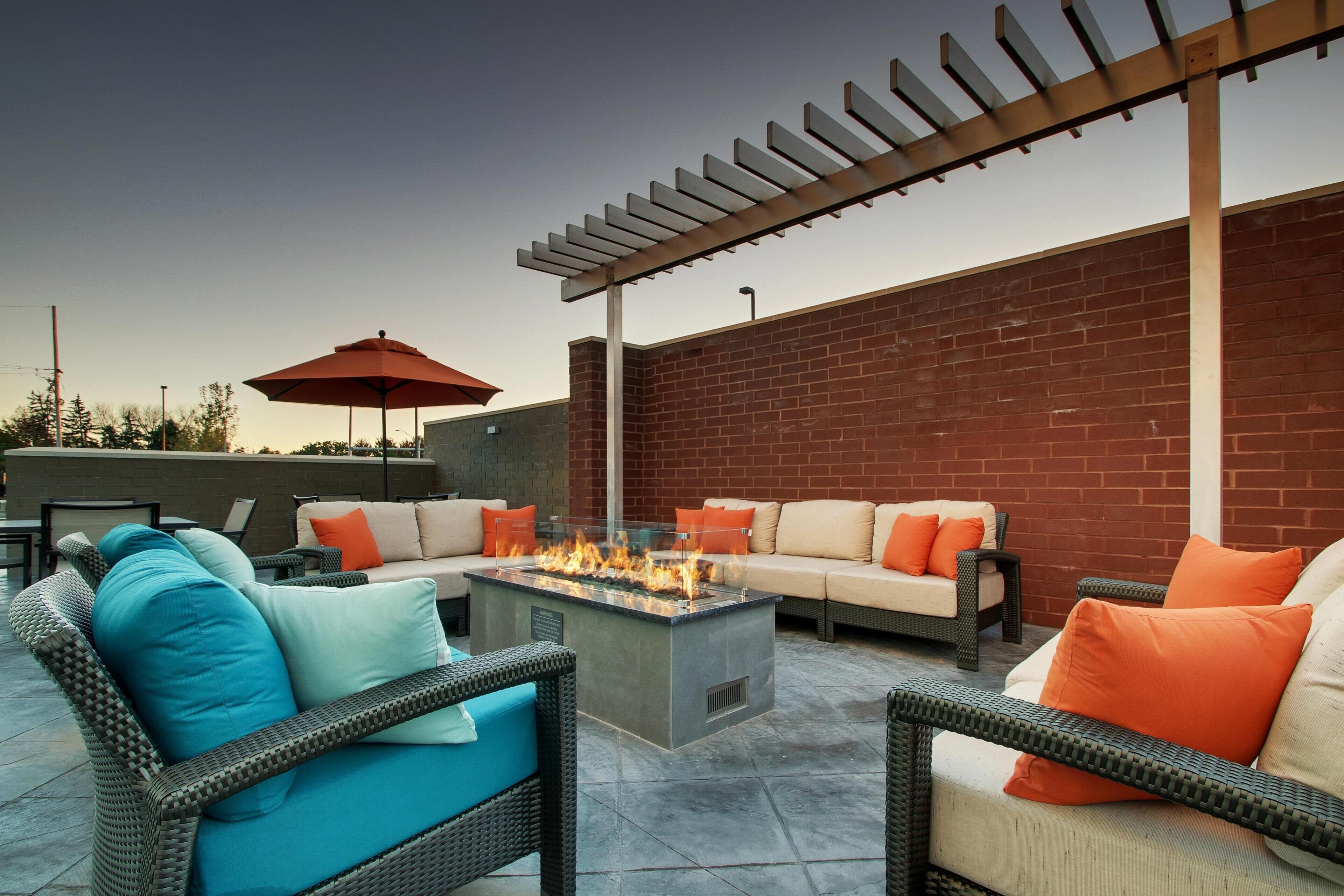 An outdoor patio area with a fire pit, wicker furniture, and a brick wall.