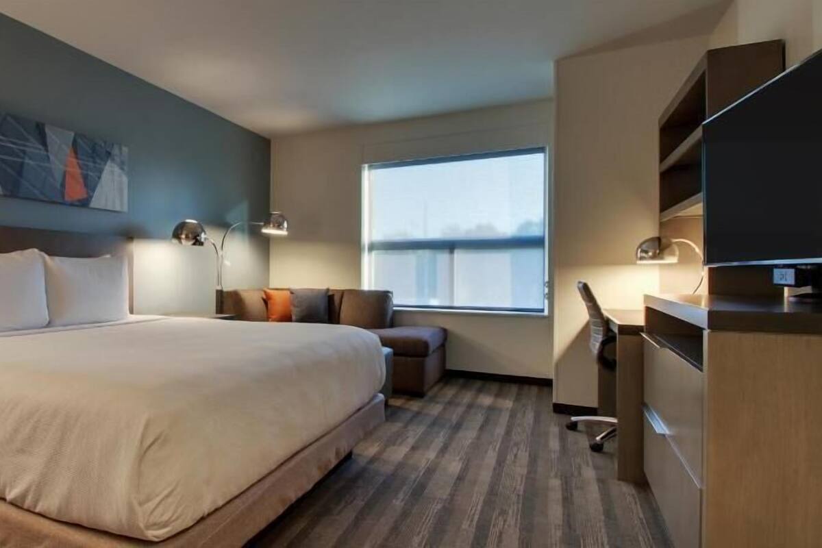 A hotel room with a bed, a desk, a chair, a TV, and a window with a view.