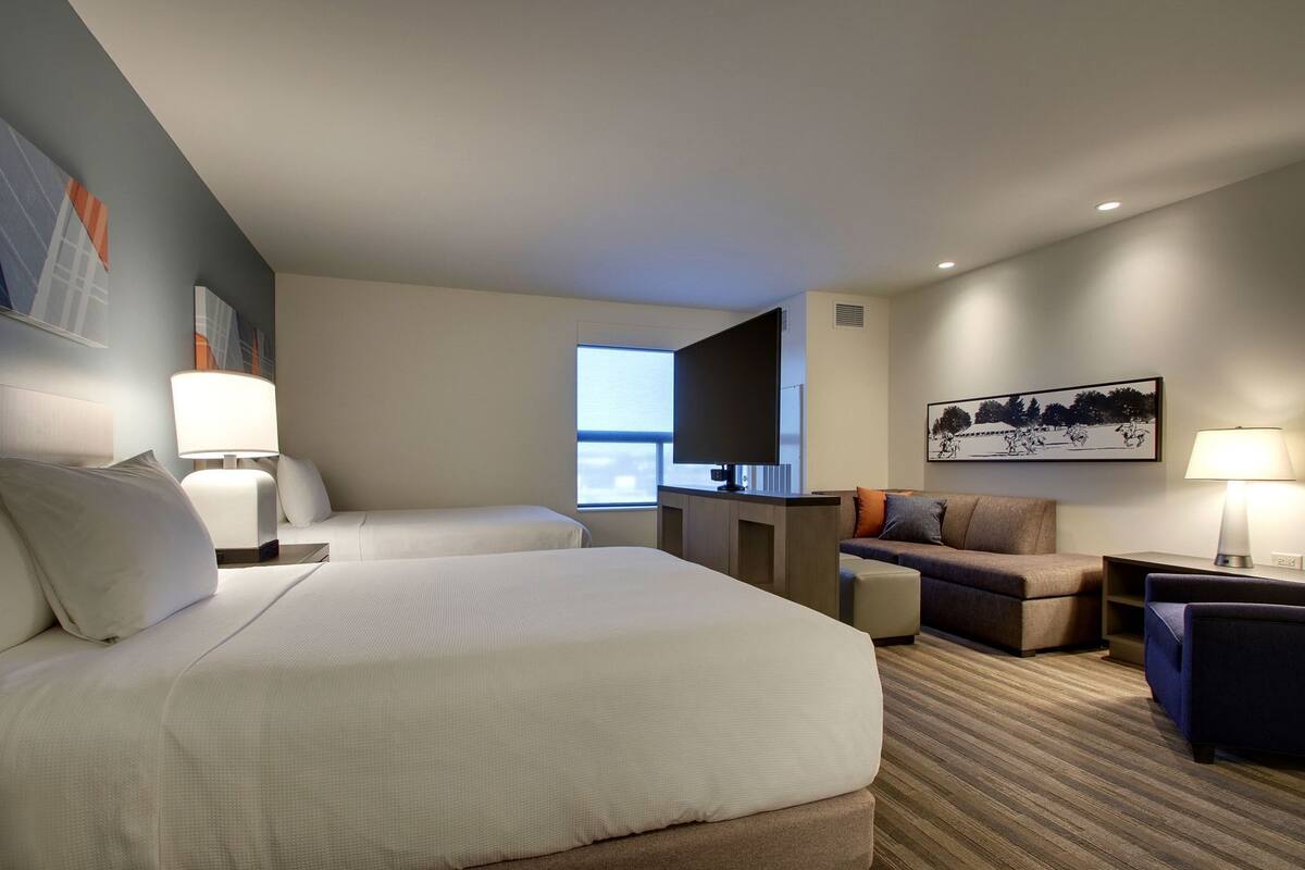A hotel room with two beds, a desk, a sofa, and a TV.