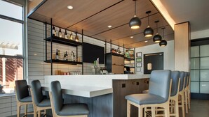 A modern bar area with a central island, bar stools, shelves with bottles, and pendant lighting.