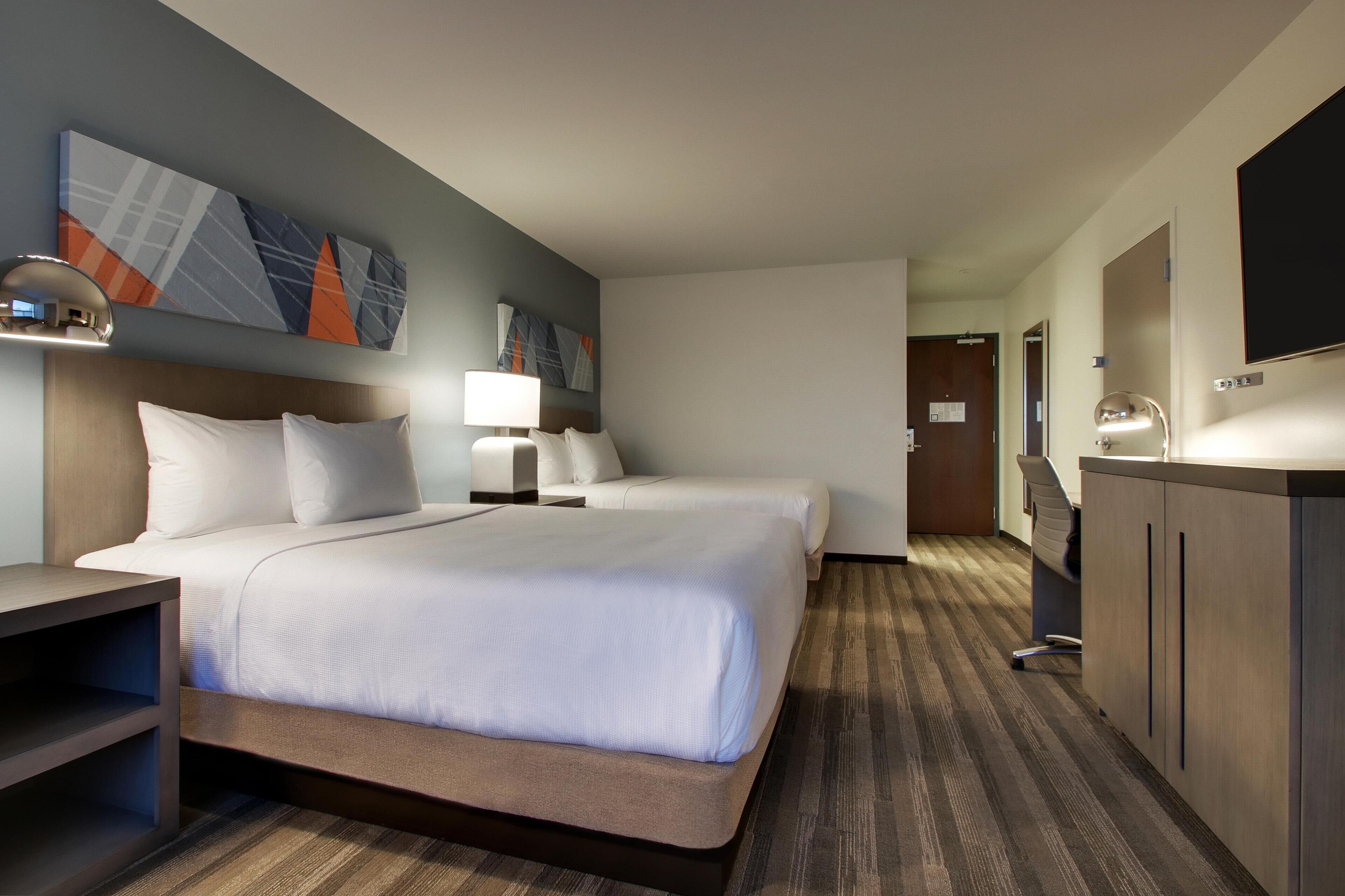 A hotel room with a large bed, two bedside tables with lamps, a desk, and a wardrobe.
