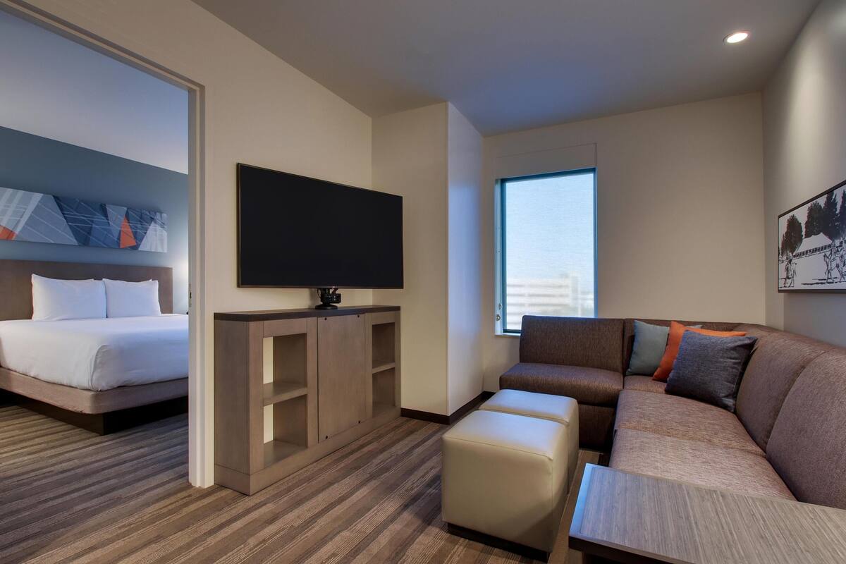 A hotel room with a bed, a TV, a sofa, and a window.