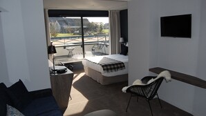 Quarto de hotel moderno com cama, escrivaninha, cadeira e varanda com vista para o exterior.