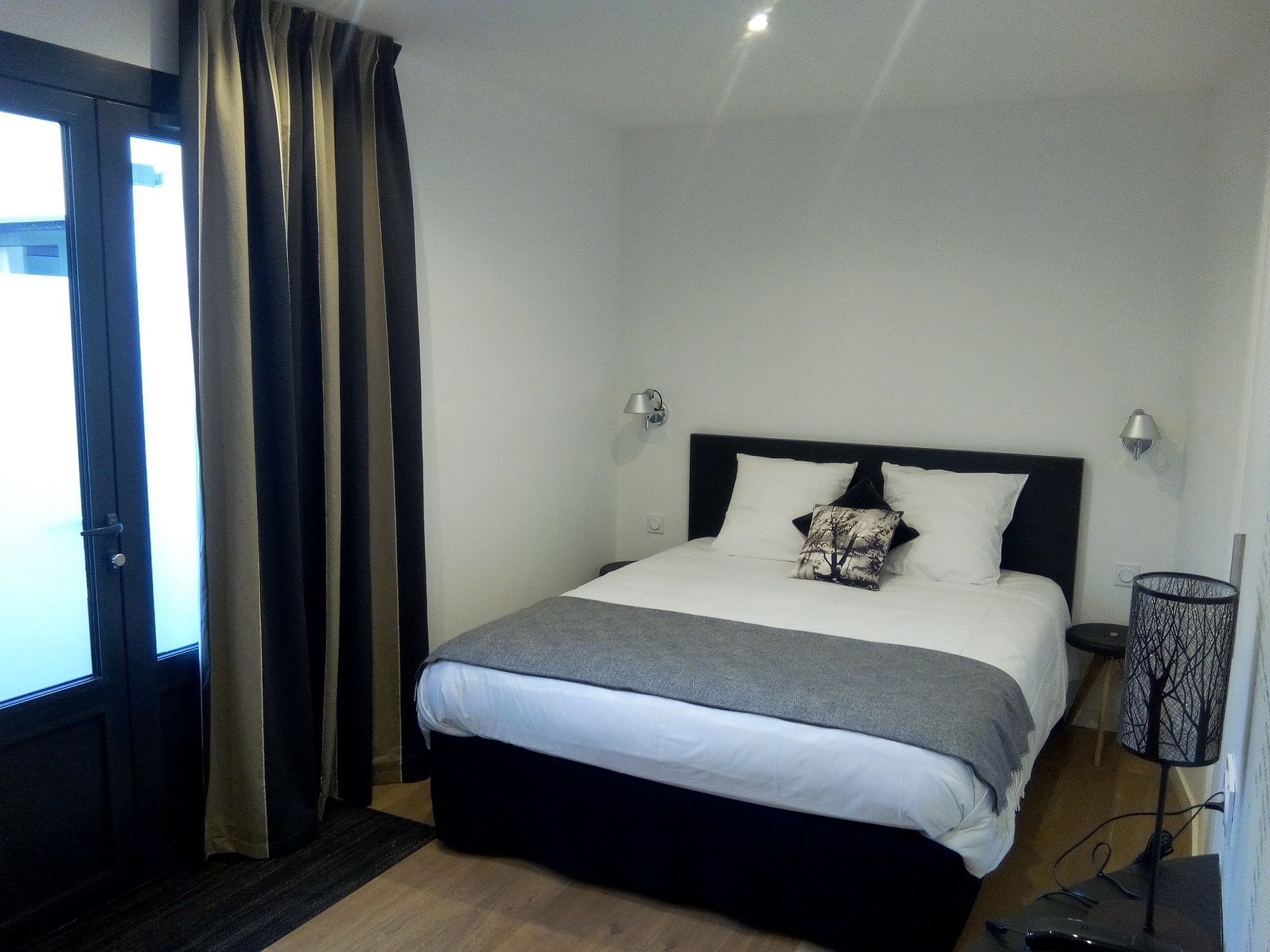 A bedroom with a bed, a nightstand, a lamp, and a window with curtains.