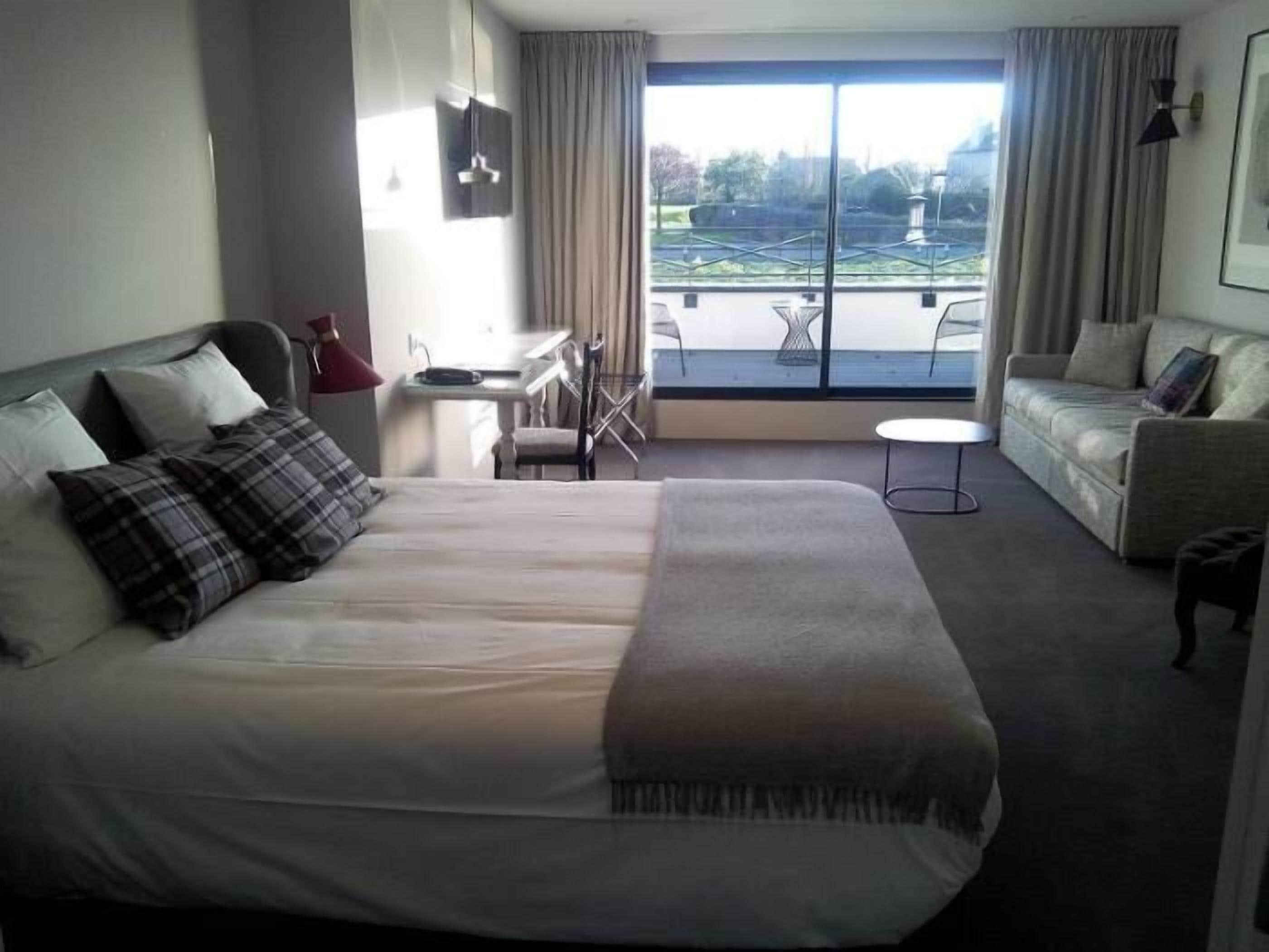 Habitación de hotel con una cama grande, un sofá, una mesita y un balcón con vistas.