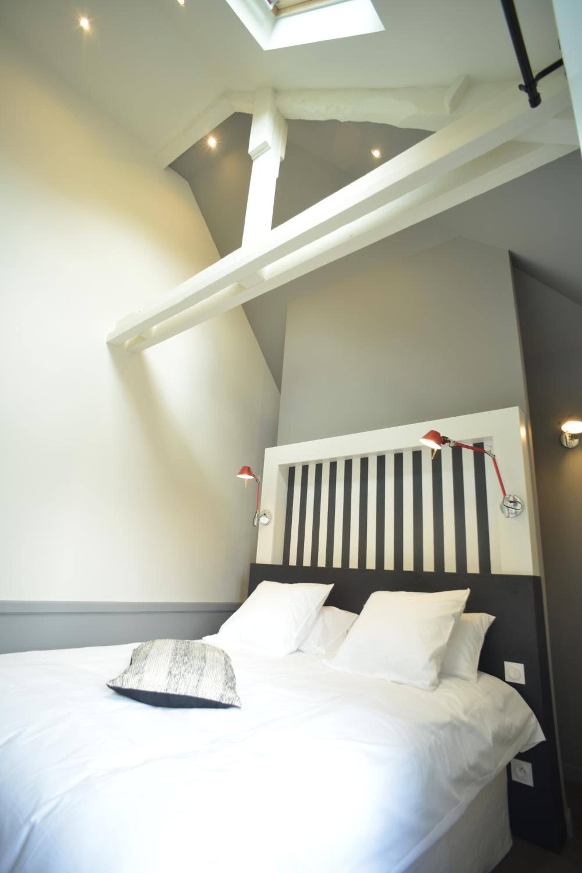 A bedroom with a sloped ceiling, a bed with white bedding, a striped headboard, and two wall-mounted reading lamps.