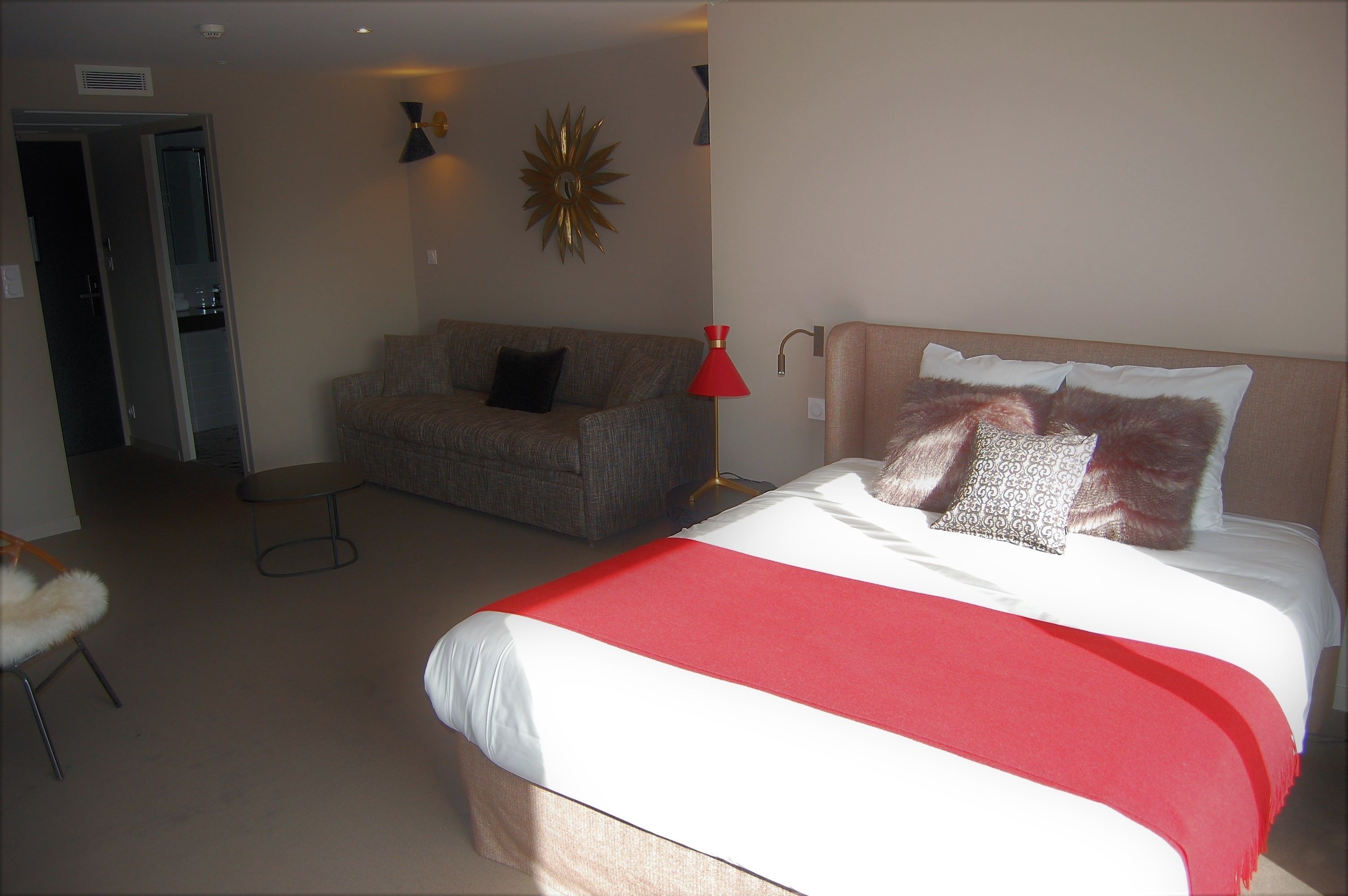 Een slaapkamer met een bed, een bank, een rode vloerlamp en een wanddecoratie.