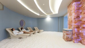 Een kamer met een groot bed bekleed met witte lakens, een bakstenen muur en een plafond met inbouwverlichting.