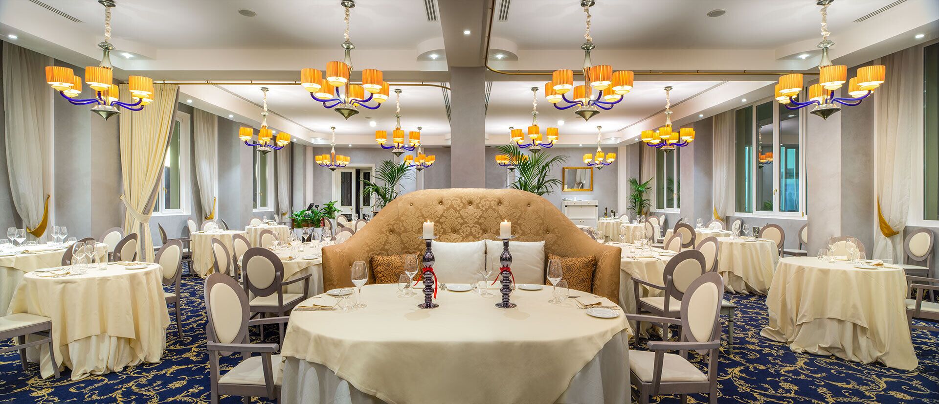 Un comedor elegante con mesas redondas, sillas, candelabros y un amplio sofá tapizado.