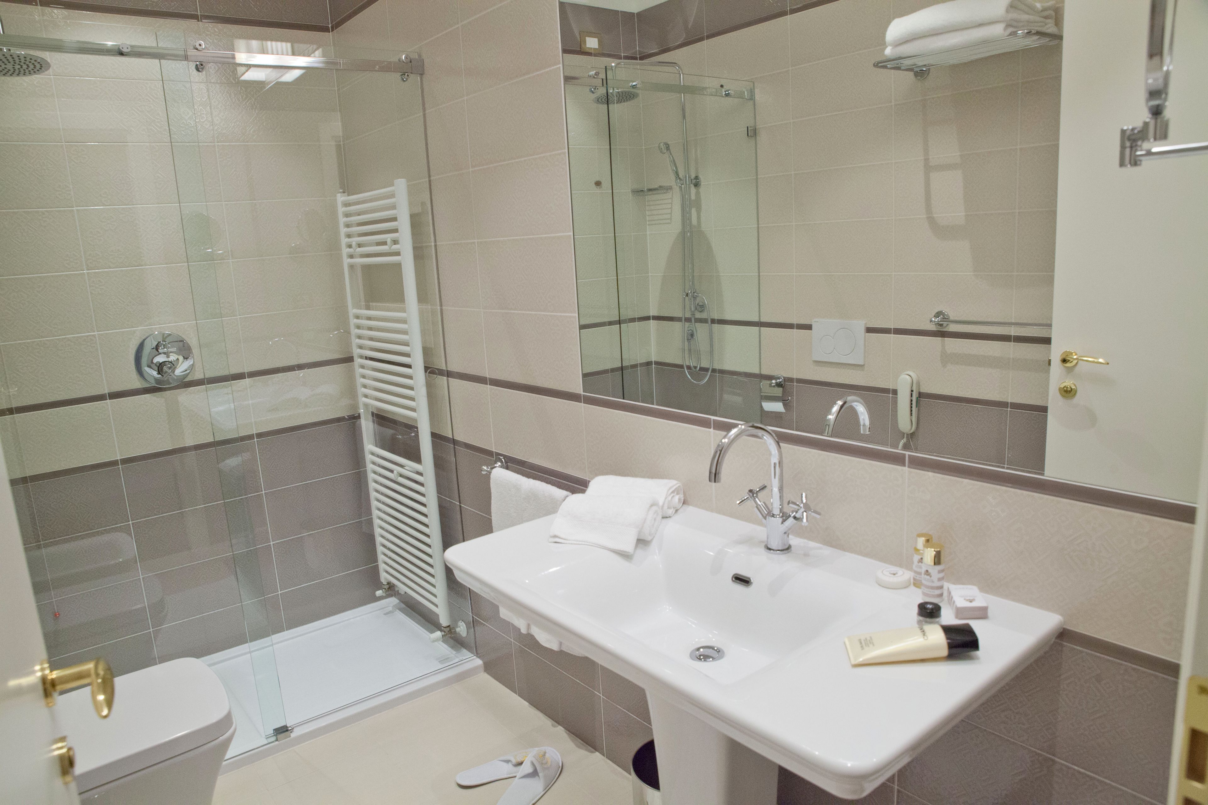Un baño moderno con ducha de vidrio, lavamanos blanco y artículos de aseo, y un espejo grande.