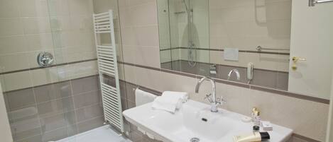 Un baño moderno con ducha de vidrio, lavamanos blanco y artículos de aseo, y un espejo grande.