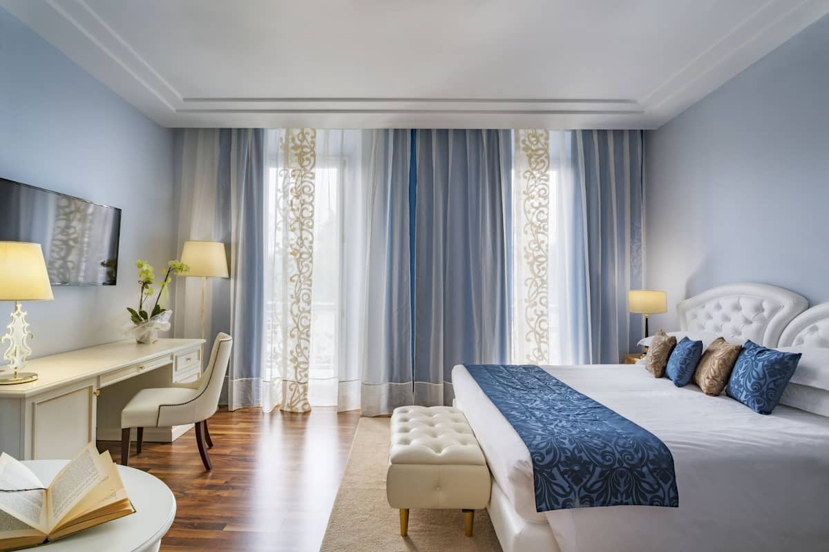 Een hotelkamer met een bed, een bureau, een stoel, een lamp en een raam met gordijnen.