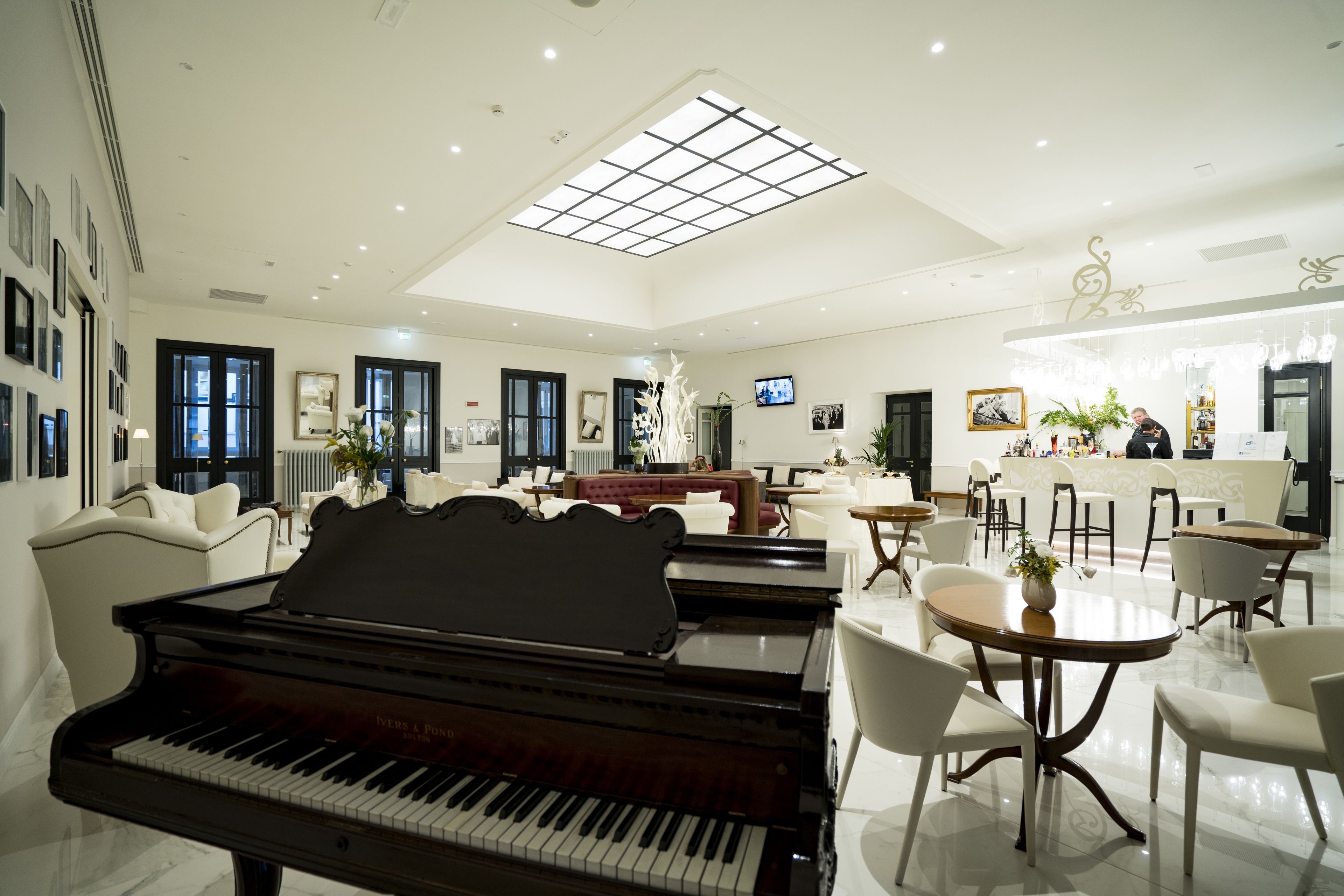 A spacious living room with a grand piano, a dining area with round tables, and a bar area with a counter.