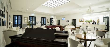 A spacious living room with a grand piano, a dining area with round tables, and a bar area with a counter.