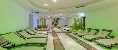 A spa room with multiple massage tables arranged in rows, a wooden floor, and a ceiling with recessed lighting.