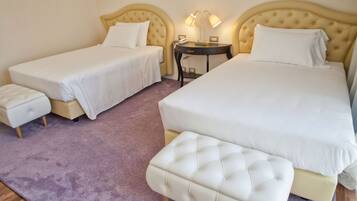 Una camera d'albergo con due letti singoli, un letto matrimoniale, un comodino con lampade e un pouf coordinato.