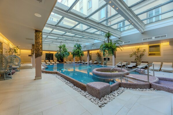 Una piscina interior con techo de vidrio, sillas de descanso y plantas en macetas.