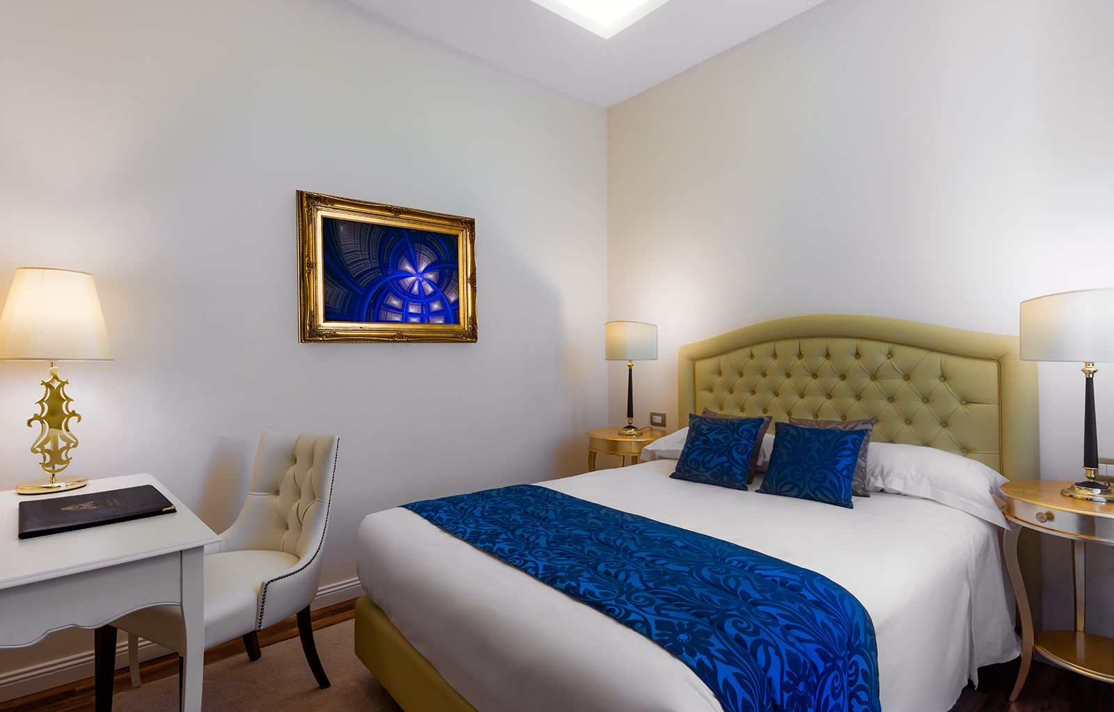 A hotel room with a large bed, a desk, a chair, and a painting on the wall.