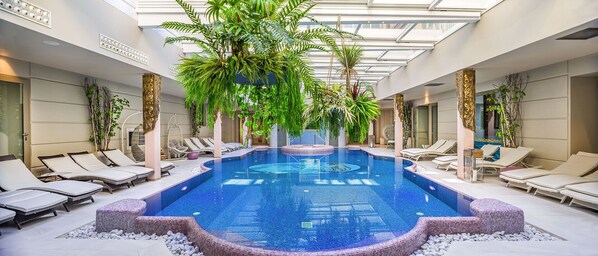 Una piscina interior con sillones de descanso y plantas tropicales.