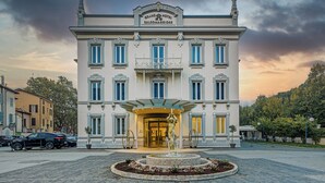 Een statig hotel met een centrale ingang, een fontein en een verzorgde tuin.