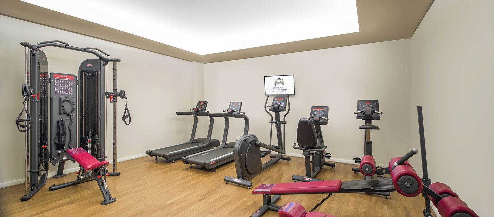 Ein Fitnessstudio mit Laufbändern, Krafttrainingsgeräten und einer roten Hantelbank.
