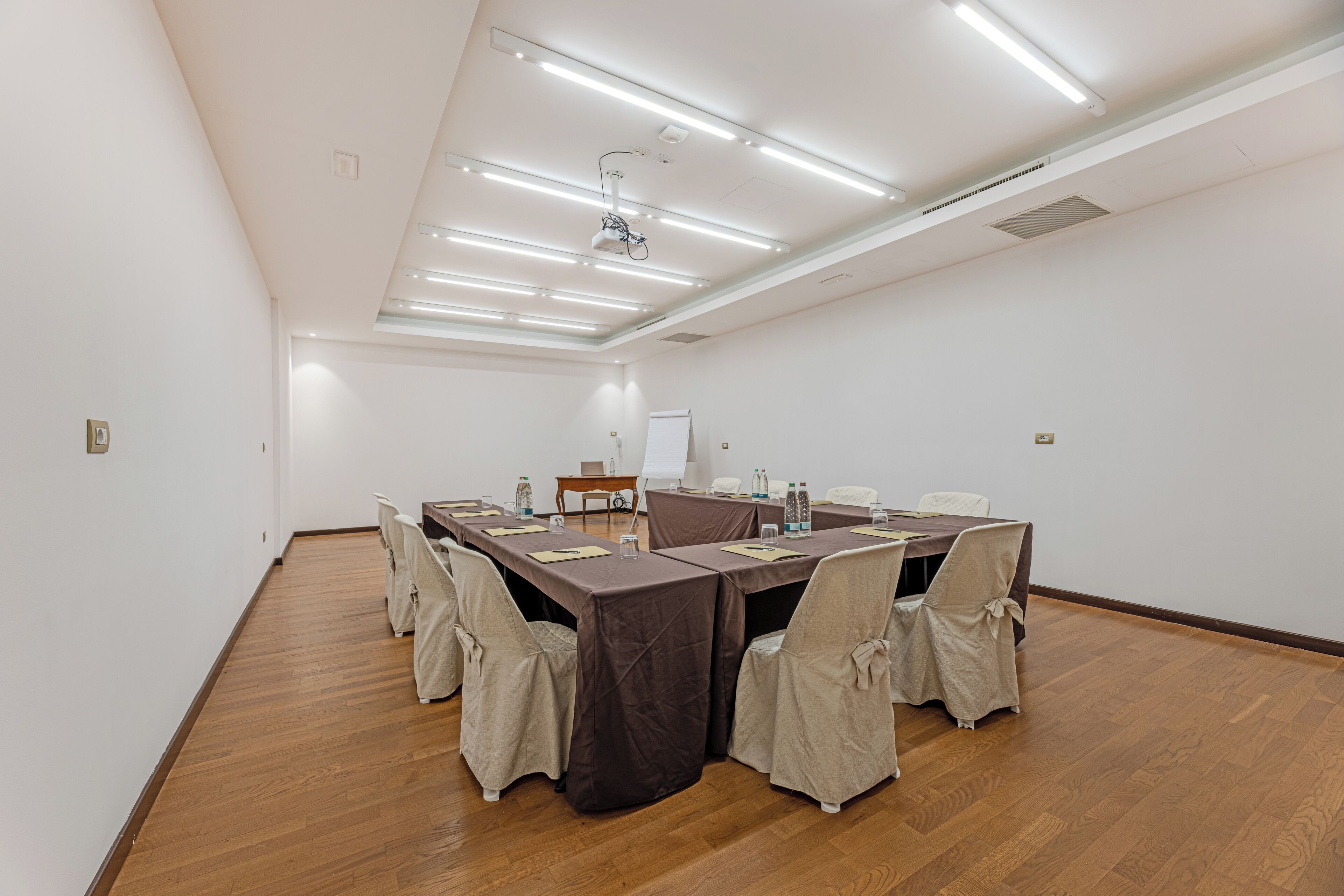 Un salón de conferencias con una larga mesa, sillas, un proyector y una pizarra.