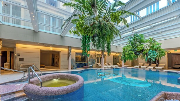 Een binnenzwembad met een jacuzzi, ligbedden en kamerplanten.