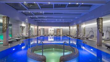 A modern indoor swimming pool with a central hot tub, surrounded by lounge chairs and a ceiling with skylights.