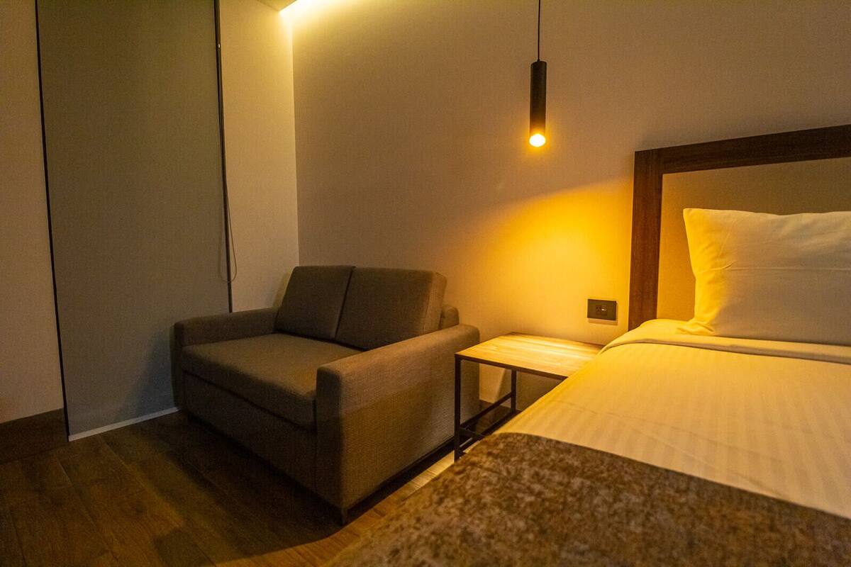 Ein Hotelzimmer mit Bett, Sessel, Nachttisch und Pendelleuchte.