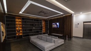 Uma sala de estar moderna com um sofá cinzento, prateleiras embutidas com objetos decorativos, uma televisão de tela plana e uma pequena mesa.