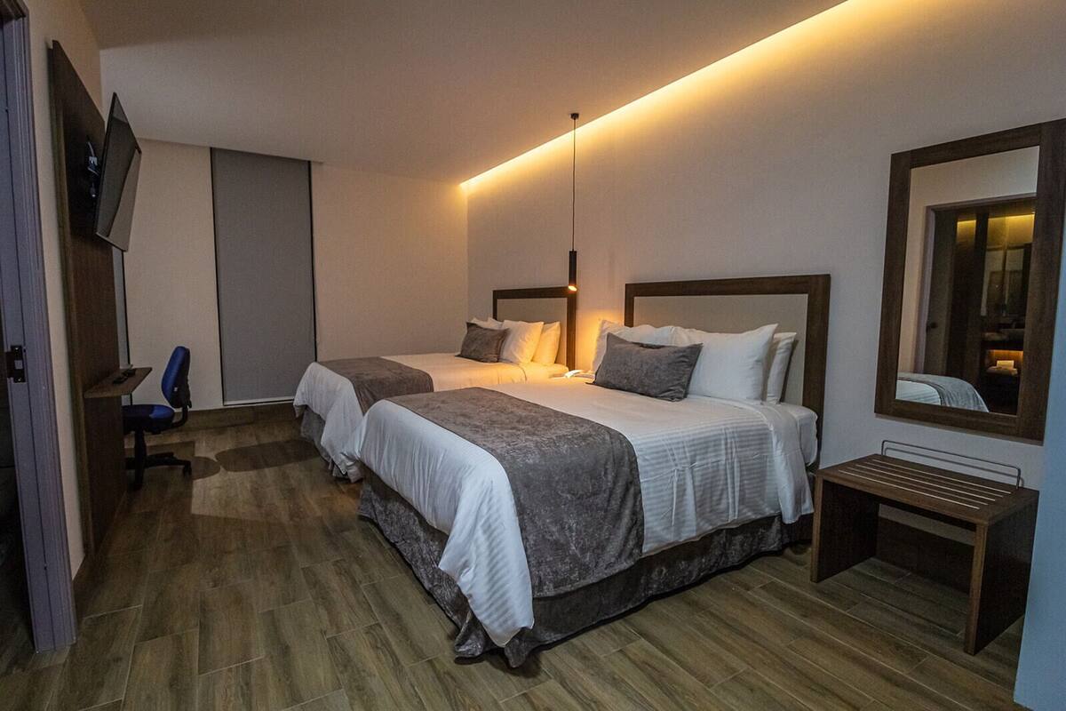 Ein Hotelzimmer mit zwei Betten, einem Schreibtisch, einem Sessel, einem Fernseher und einem Spiegel.