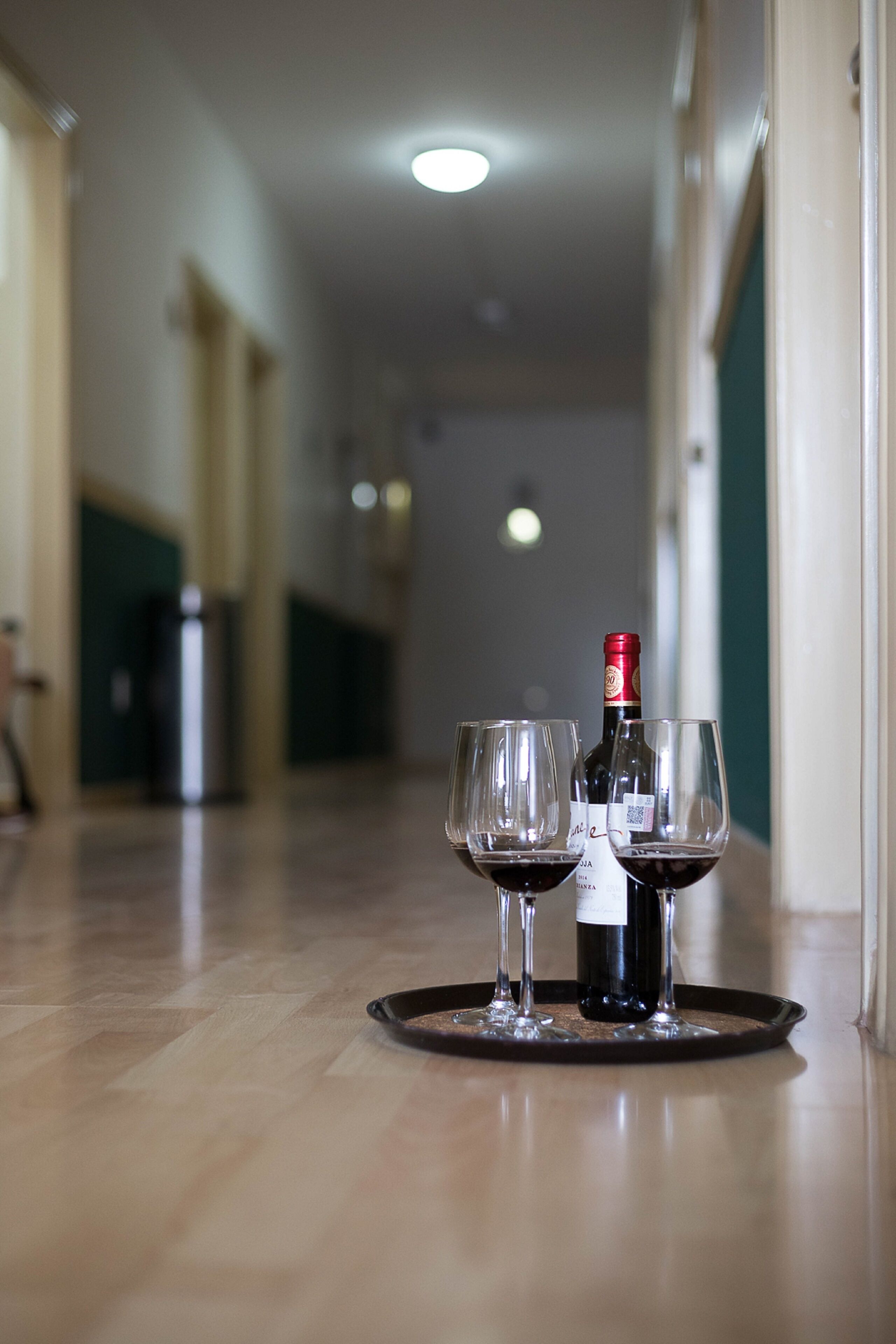 Un pasillo con una bandeja que contiene una botella de vino y dos copas en el suelo.
