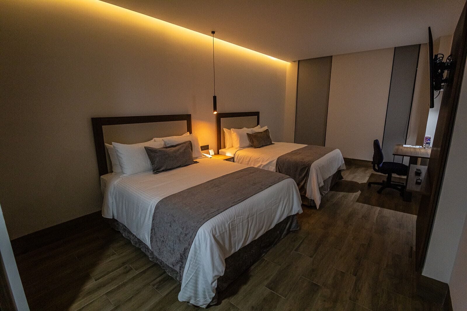 A hotel room with two beds, a desk, and a chair.