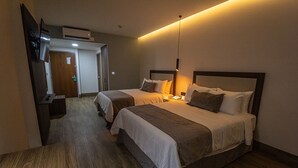 Quarto de hotel com duas camas, piso de madeira, televisão e porta para o banheiro.