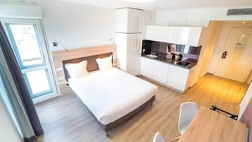 Habitació d'hotel petita amb un llit individual, una cuineta i zona de menjador.