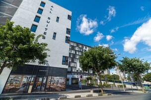 Un moderno edificio de hotel con letrero que dice 'ALL SUITES', una entrada visible y un cielo despejado.